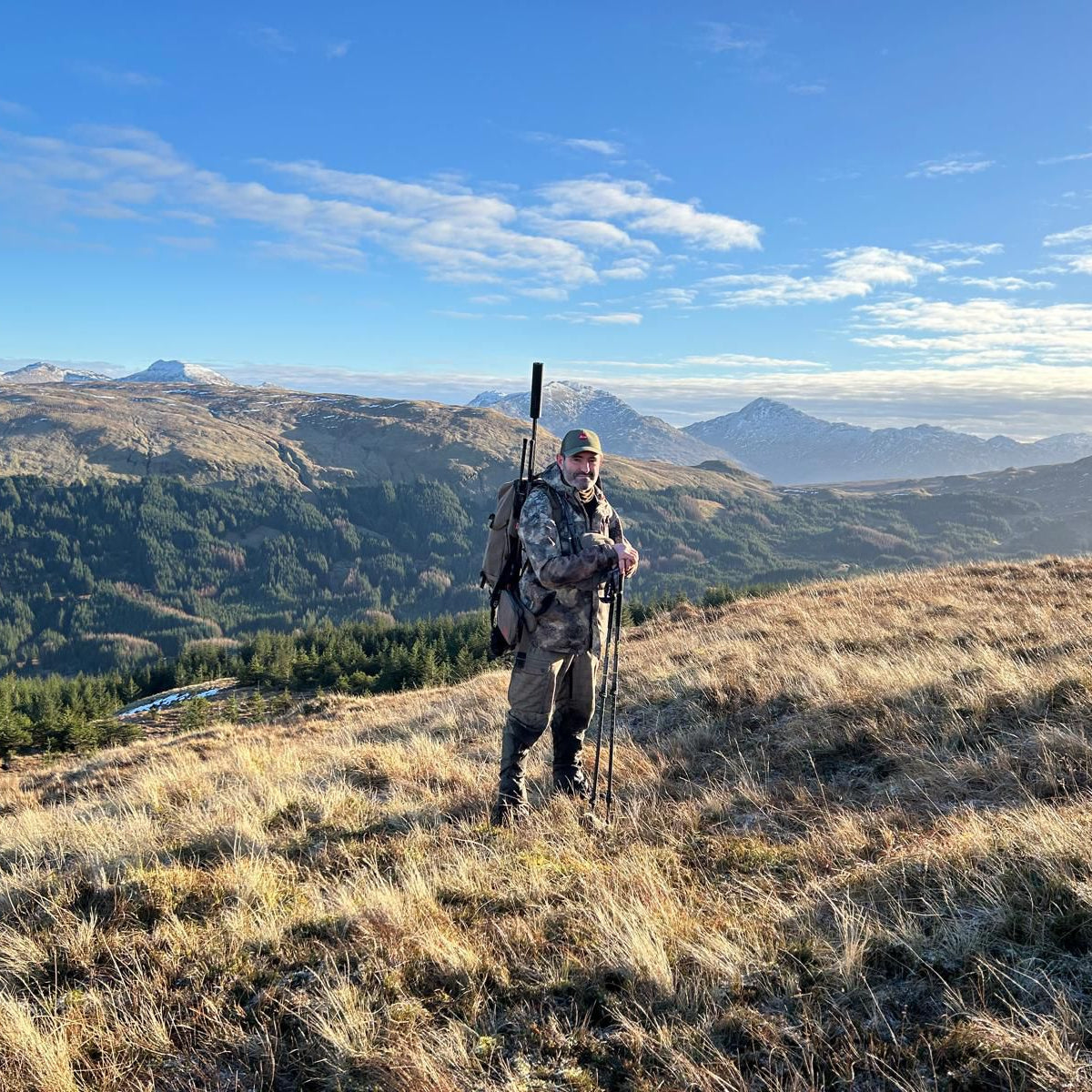 Person in camouflage gear with hunting equipment standing on a mountain with scenic view